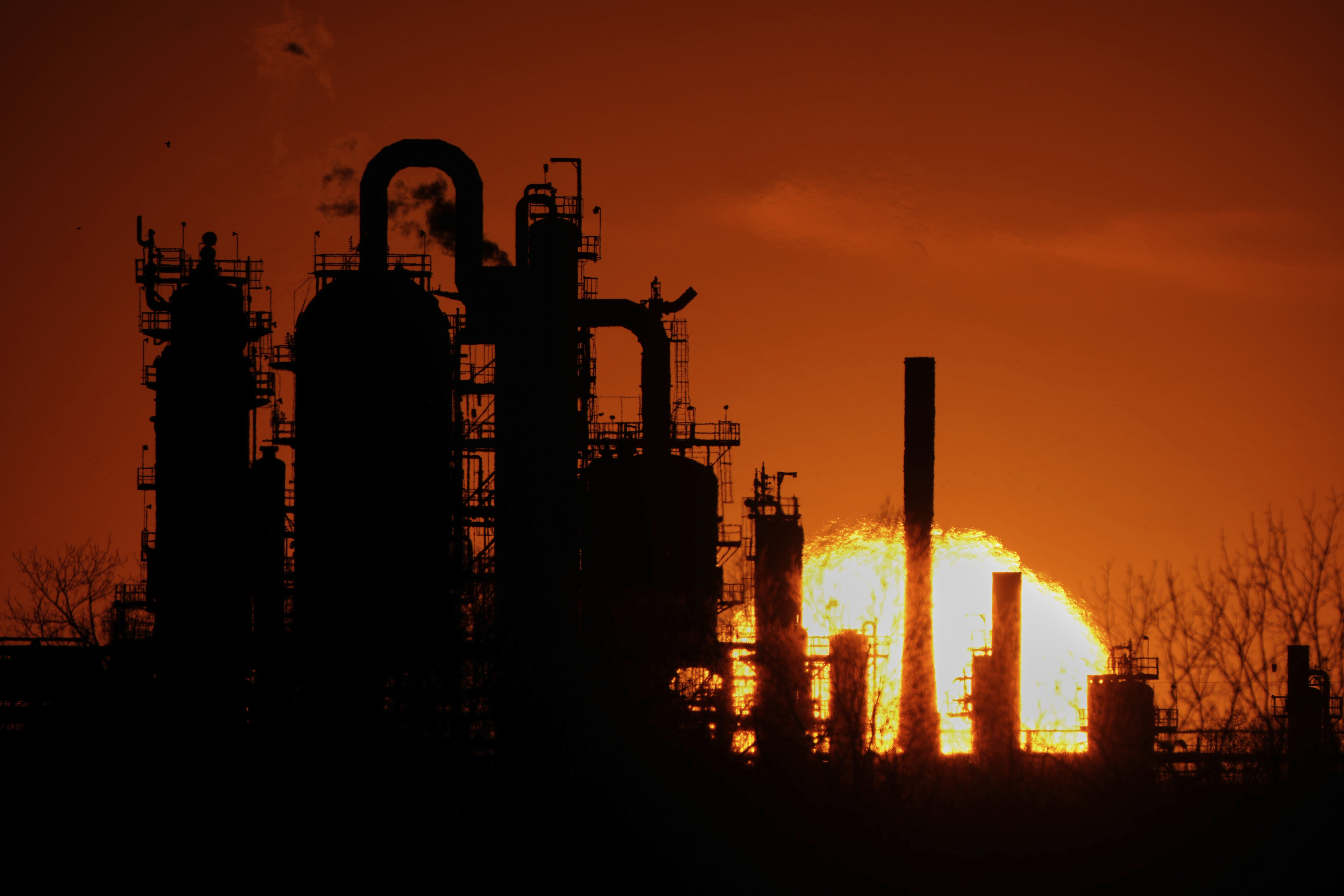 An oil refinery is silhouetted against the sky. An oil refinery is silhouetted against the sky.