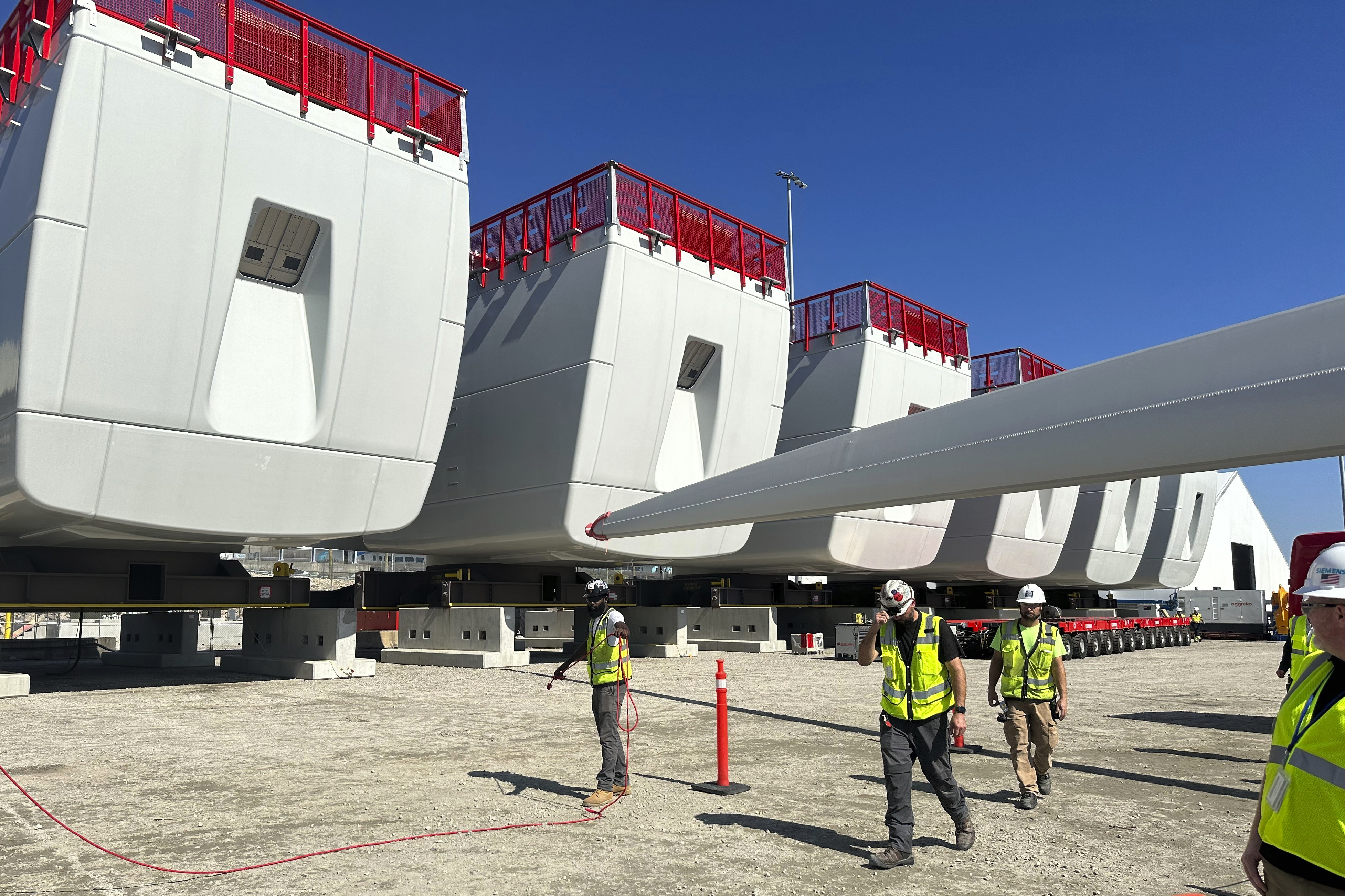 Workers walk by components of wind turbines being assembled at the State Pier in New London, Connecticut. 